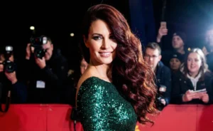 A woman with glamorous, long dark red wavy hair swept over her shoulder, posing on a red carpet at night