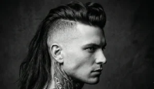 A high-contrast black and white profile photograph of a man with shaved sides, a tall dark pompadour on top, and long hair hanging down his back. Image 5: A high-contrast black and white profile photograph of a man with shaved sides, a tall dark pompadour on top, and long hair hanging down his back.
