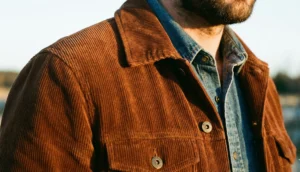 A close-up view of a rust-colored corduroy jacket worn over a denim shirt, showing the fabric texture under golden hour light