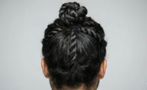 A rear close-up view of a man's head, showing an intricate twisted man bun where sections of dark hair are twisted before being tied.