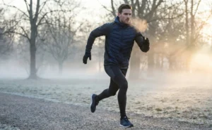 An action shot of a fit man running in a misty park during winter, wearing a hybrid hybrid puffer and knit sports jacket.