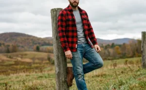 Man leaning on a fence wearing a buffalo check flannel shirt and boots for a rugged casual fall look.