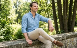 Man sitting outdoors wearing a chambray shirt and chinos with loafers, a relaxed refined outfit example.