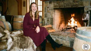 Burgundy wrap dress and heeled boots worn by a woman sitting near a winery fireplace.