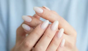 A soft-focus shot of clasped hands featuring long, oval nails with a semi-opaque, milky white finish that has a subtle pearlescent shimmer.