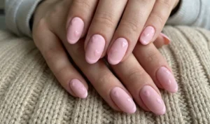 A close-up of oval nails showing a textural contrast. The base is a flat matte baby pink, while subtle hearts and thin French tips are painted over it using a high-shine glossy topcoat in the same shade.