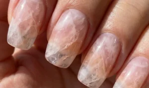 A detailed macro shot of nails designed to mimic raw rose quartz stone. Swirling layers of sheer pink, translucent white, and peach create a cloudy, fractured mineral appearance with a smooth finish.