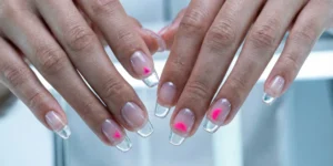 A futuristic photograph of long, sculptured nails made of clear builder gel that looks like glass. Suspended within the clear layers are small neon pink geometric shapes, including a triangle and a semi-circle.