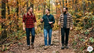 10. Rugged Casual

Three men on a wooded trail in autumn. They are wearing flannel checked shirts (Buffalo plaid, Green/Navy tartan, and Brown check) with rugged denim and heavy-duty leather boots. Natural soft forest lighting.

