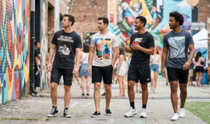 A candid photo of four distinct men showcasing variations of graphic t-shirts and black shorts while exploring a vibrant outdoor street art festival.