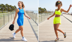 Two women in athletic sets are featured on a modern boardwalk. The left woman in an electric blue ribbed set holds a mini backpack. The right woman in a neon yellow sports bra and running shorts wears colorful accessories and sandals.