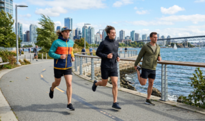 A dynamic natural daylight photograph capturing three men on a modern waterfront running path on a bright, windy day in action poses.