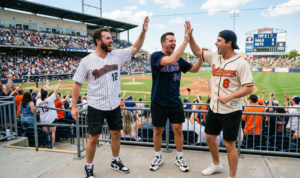 A natural daylight photograph capturing three men with dynamic, animated poses, cheering and high-fiving in a lively sports setting.