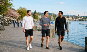A natural daylight photograph of three men enjoying a calm spring afternoon by the waterfront, strolling along a scenic promenade.