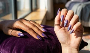 A close-up of a multi-dimensional holographic royal purple manicure reflecting a vibrant rainbow prism effect under natural light.