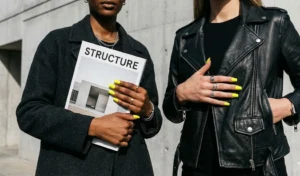A high-fashion, ultra-glossy solid cyber yellow manicure on square nails making a striking contrast against black leather streetwear.