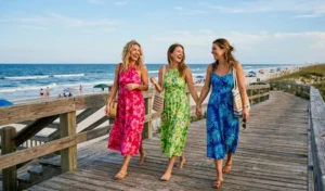 "Three women wearing colorful hibiscus print halter dresses on a wooden boardwalk."