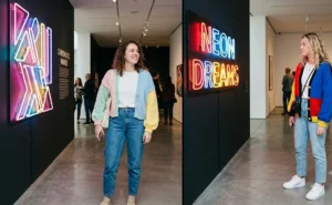 "Two women in colorful, chunky, color-blocked cardigans and vintage mom jeans observing art in a gallery, showing eclectic casual style."